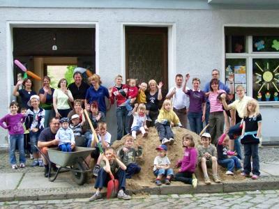 Gruppenbild Kinder und Erwachsene mit Schaufeln und Karren und einem Sanberg