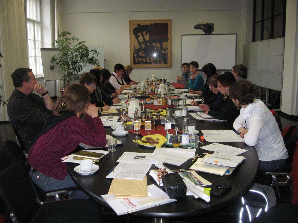 Ca. 20 Menschen in einer Beratung an einem großen ovalen Tisch
