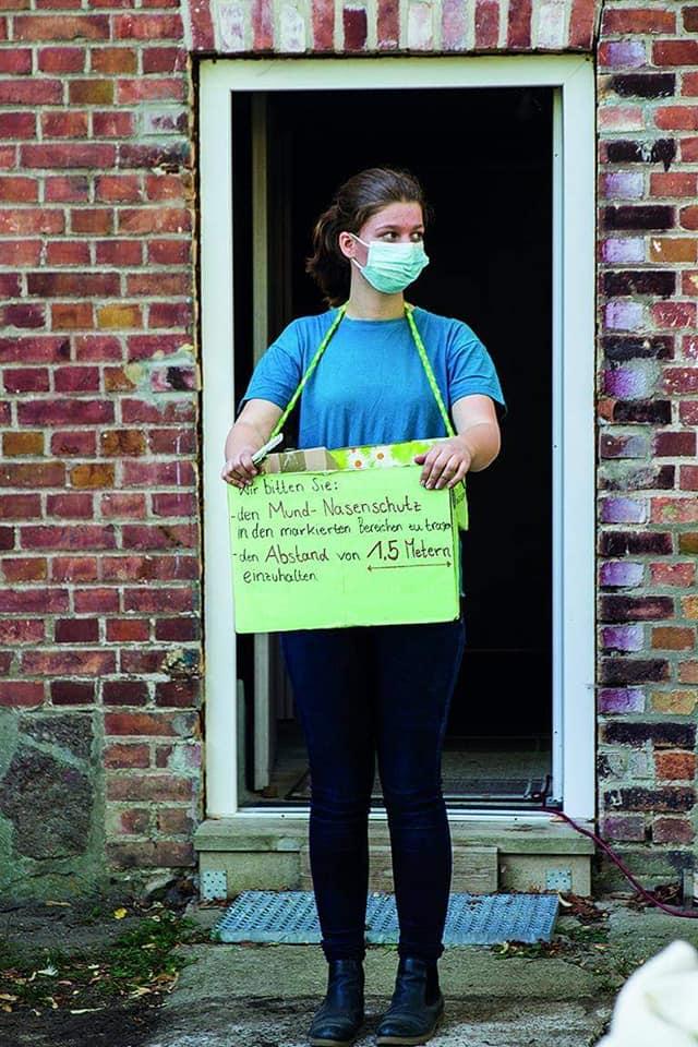 Eine Frau mit einem Schild: Bitte tragen Sie eine Maske