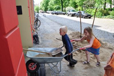 Zwei Kinder schieben eine Schubkarre mit Sand