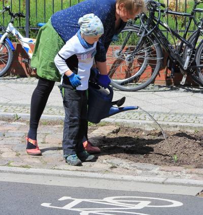eine Frau und ein Kind gießen einen Straßenbaum