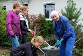 eine Seniorin arbeitet mit Jugendlichen im Garten