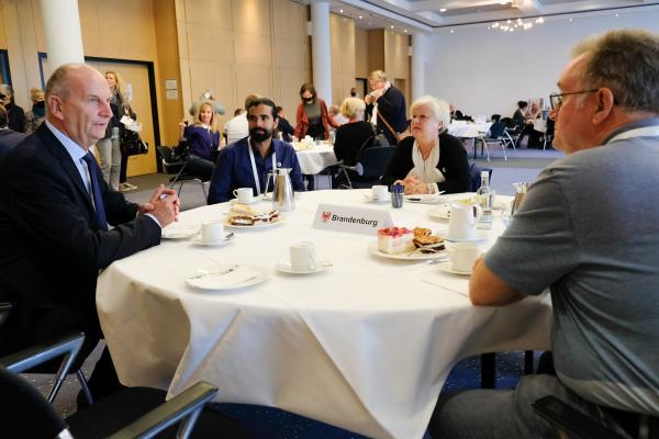 Freiwillige im Gespräch mit Ministerpräsident Woidtke an einem Kaffeetisch