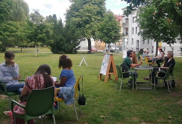 Menschen sitzen an verscheidenen Tischen im Park und unterhalten sich